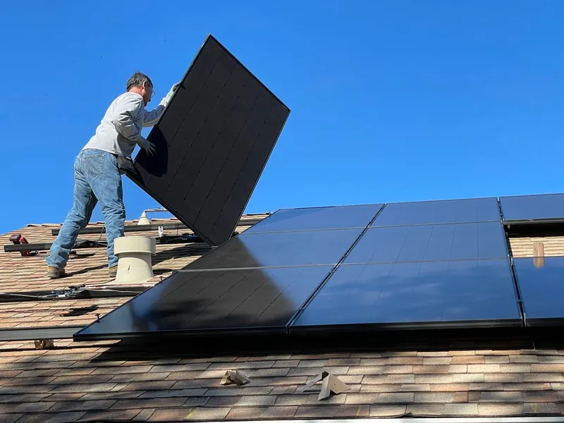Installer lifting a solar panel on a residential roof during removal and reinstall