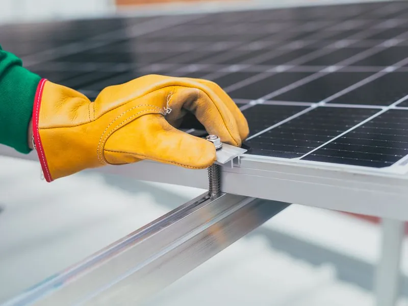 Technician in work gloves tightening a solar panel mounting clamp during repair